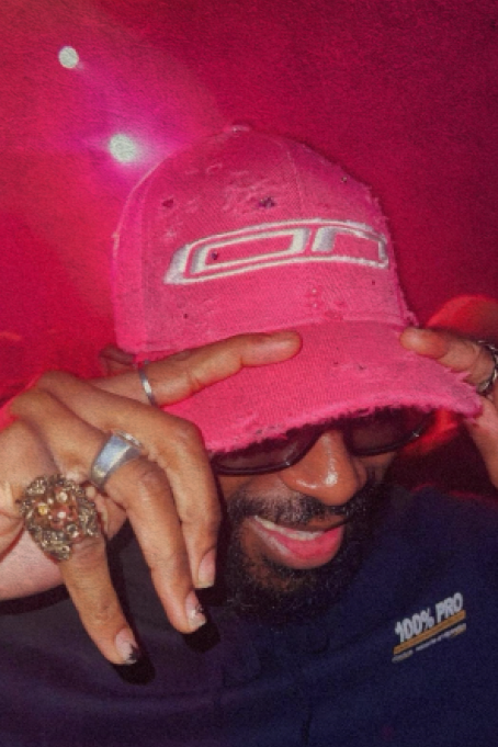 A man dons a pink hat while covering his face with his hands, conveying a sense of surprise or deep thought.